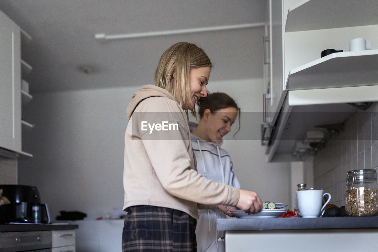 Happy young lesbians preparing meal together in kitchen at home