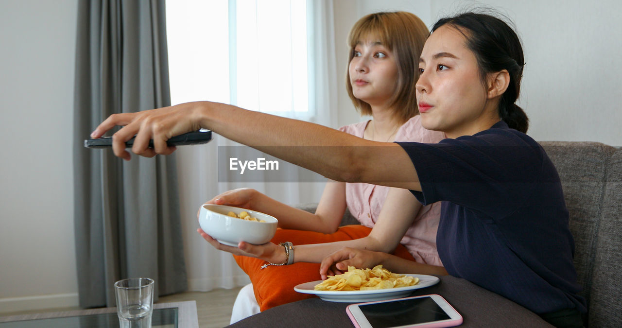 Young women watching tv while sitting with food on table