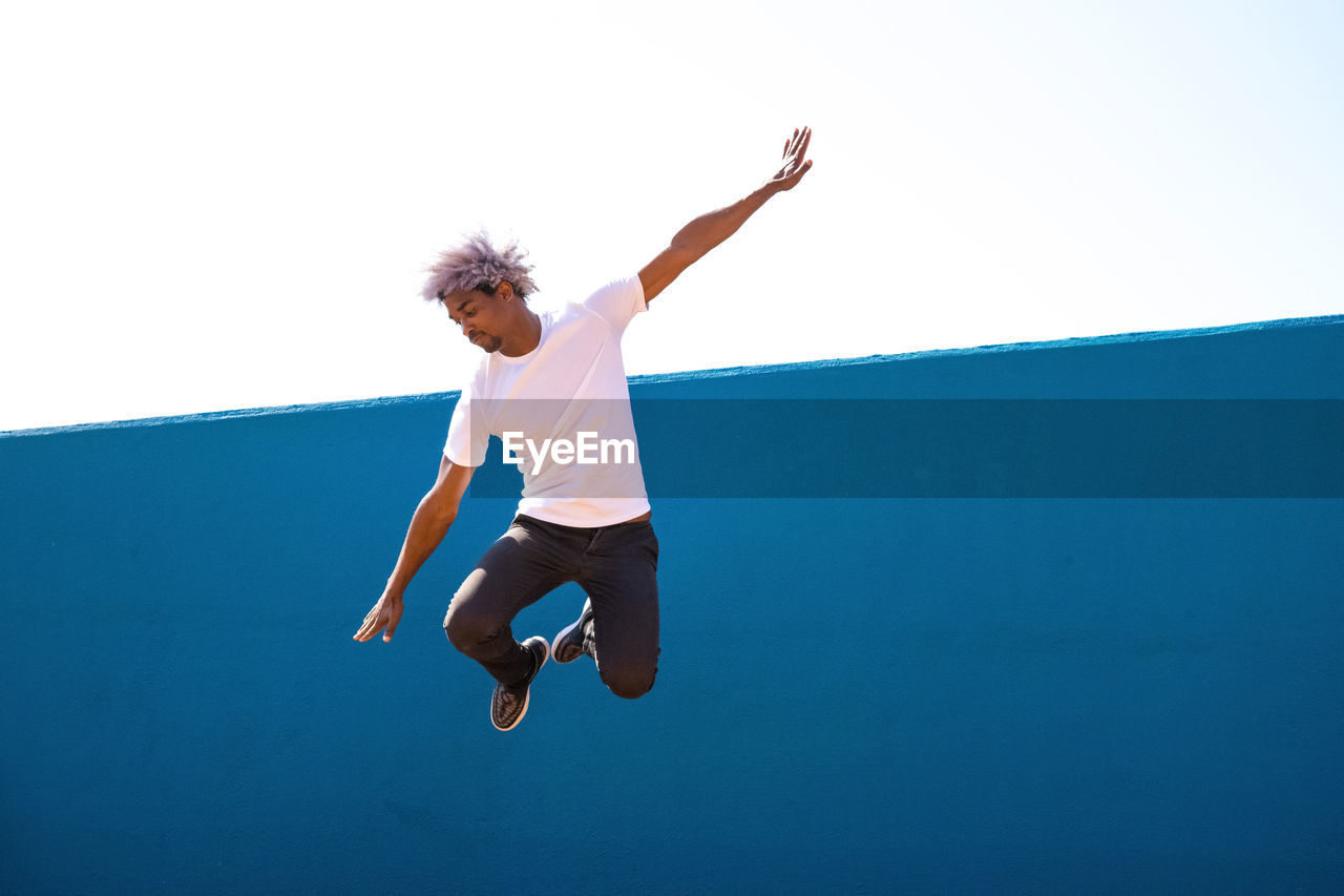 Black and afro man dressed in white jumping on a blue wall. parkour concept.