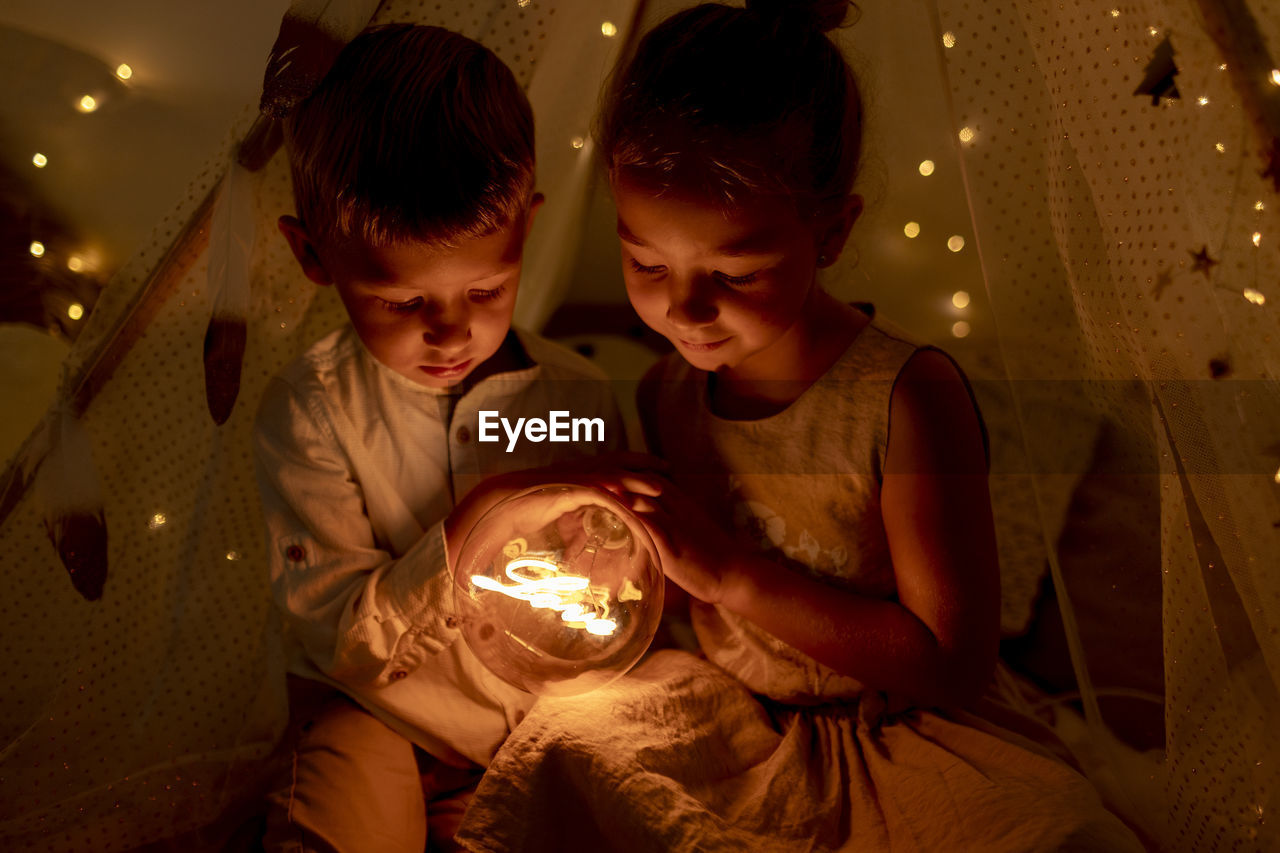 Sibling holding light while sitting in room during christmas