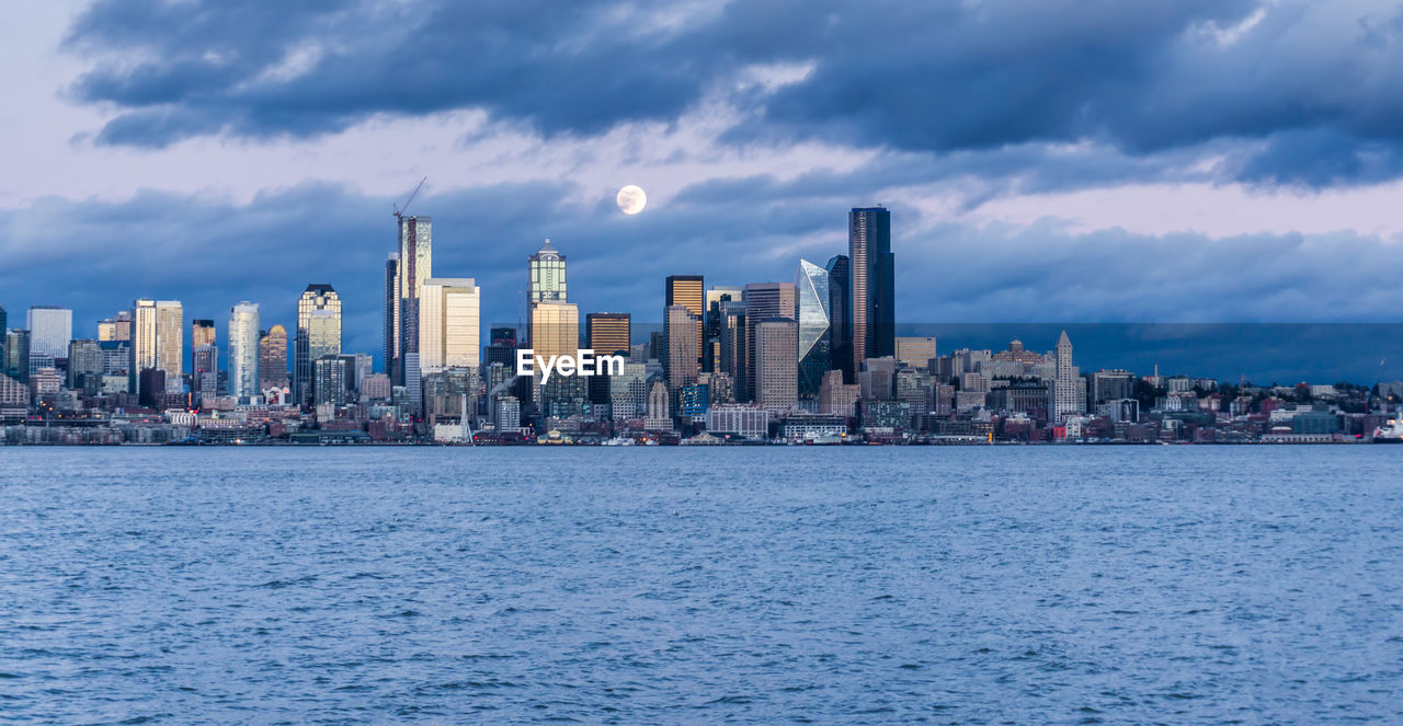 A full moon shines above the seattle skyline.