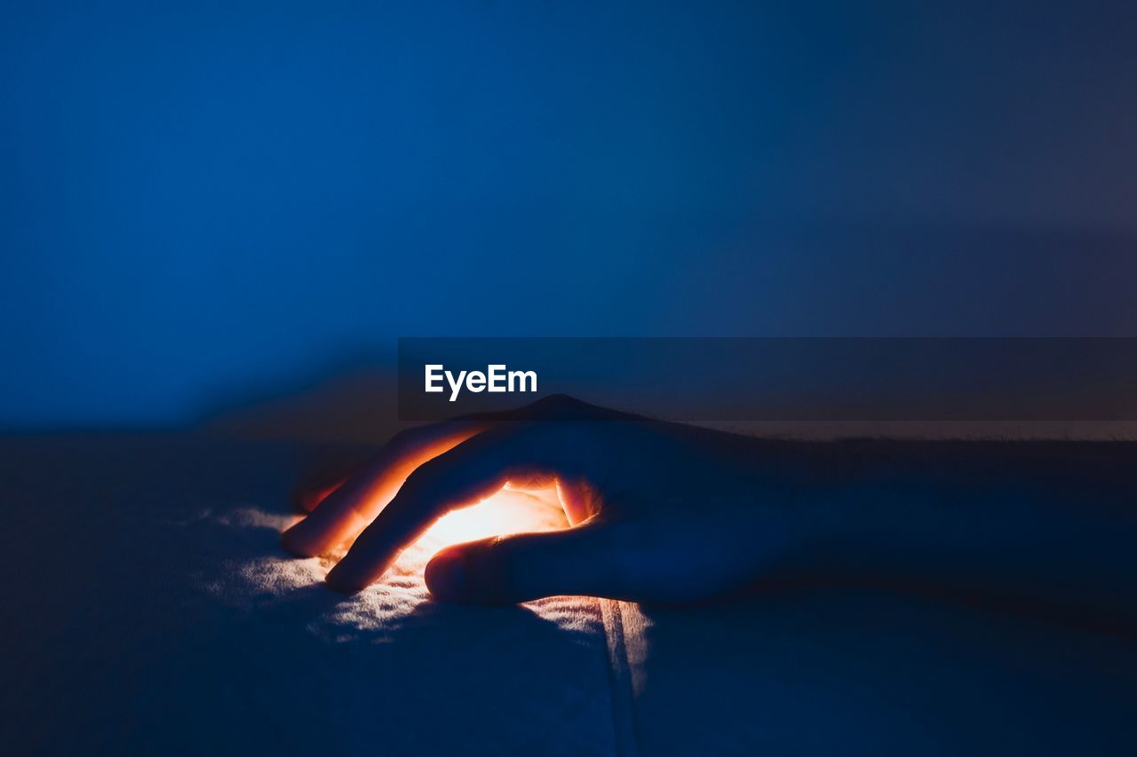 Close-up of hand covering illuminated light on sofa at night