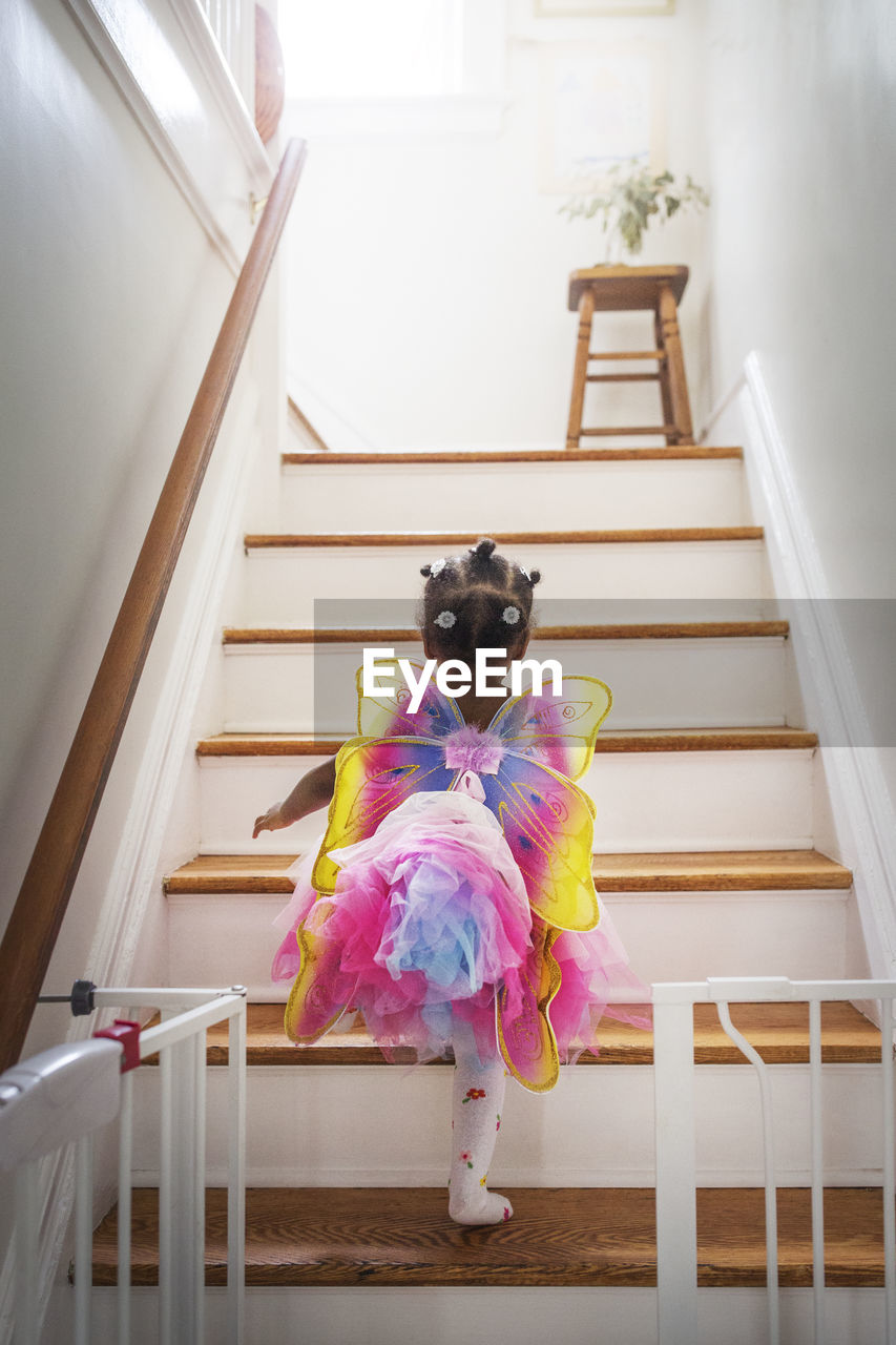 Rear view of girl dressed up in fairy costume moving up steps at home