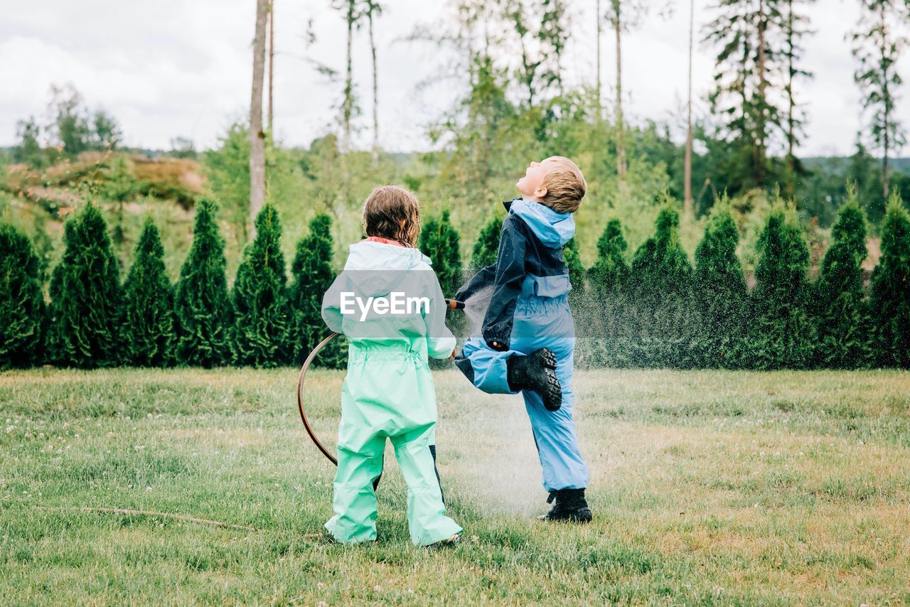 Brother and sister spraying each other with water in the yard at home