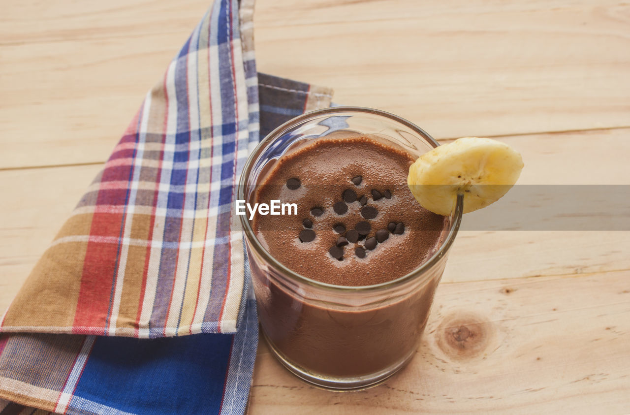 Chocolate banana smoothie topping sprinkled with chocolate chips banana slices on a wooden floor.