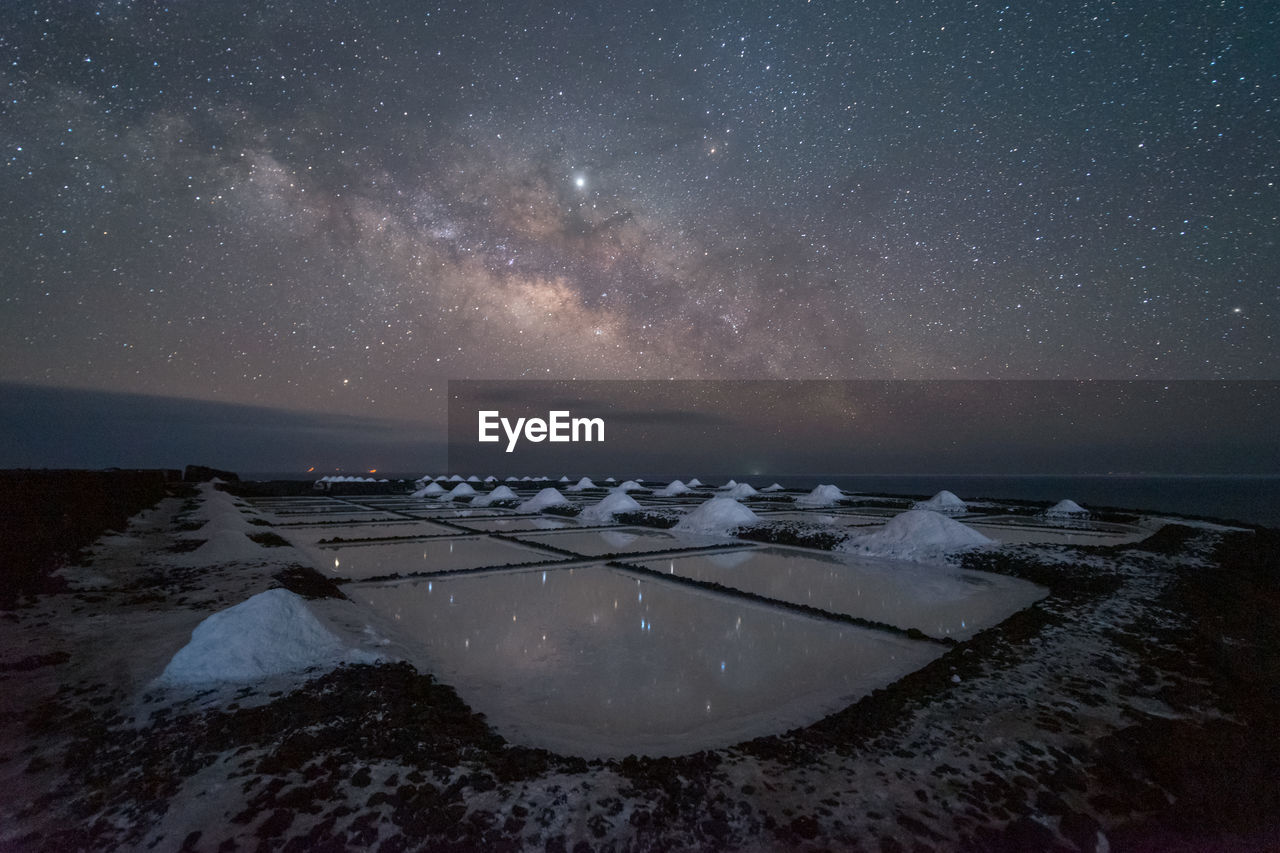 Frozen water and snow on background of spectacular seascape with milk way on starry night