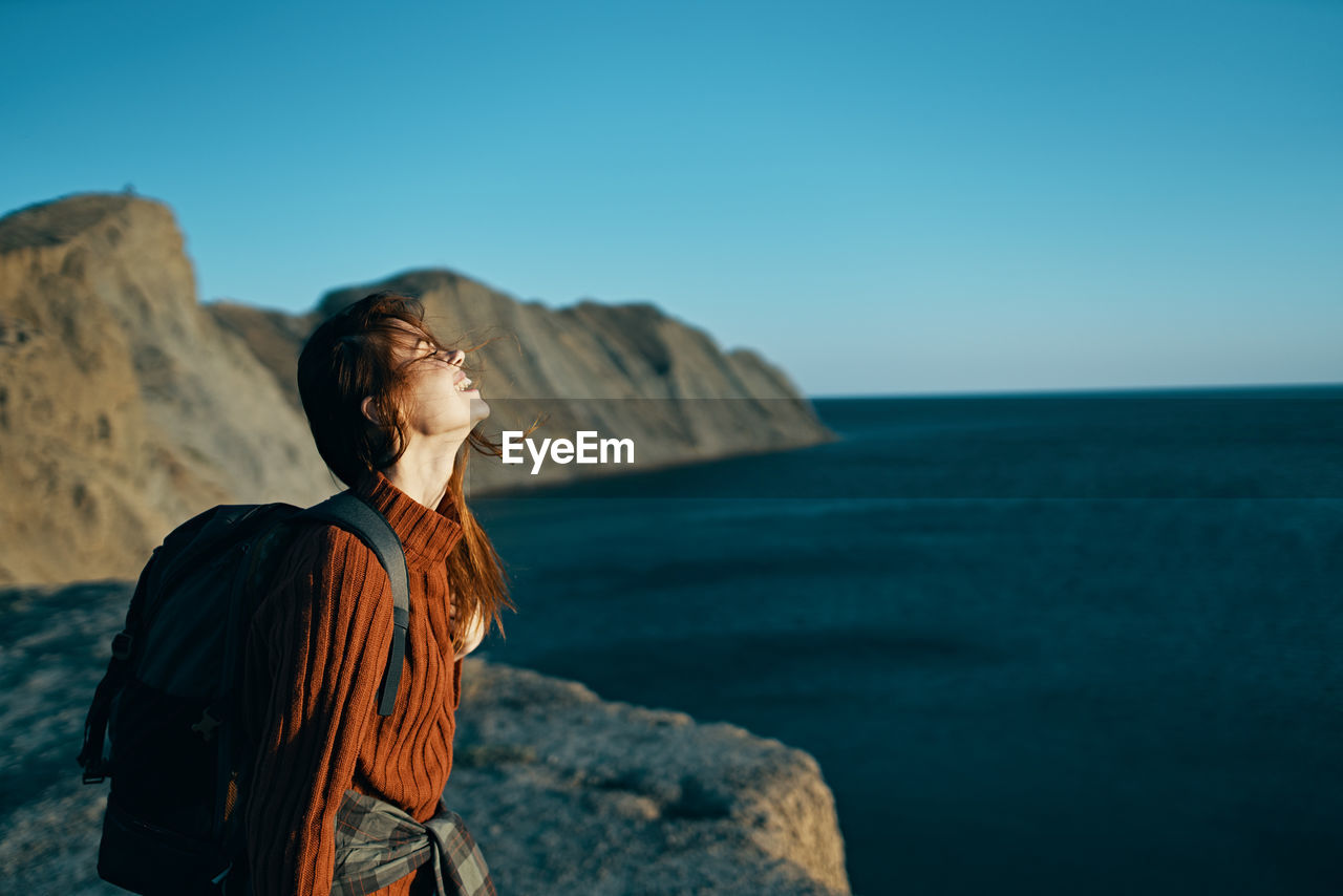 WOMAN STANDING ON ROCK AGAINST SEA