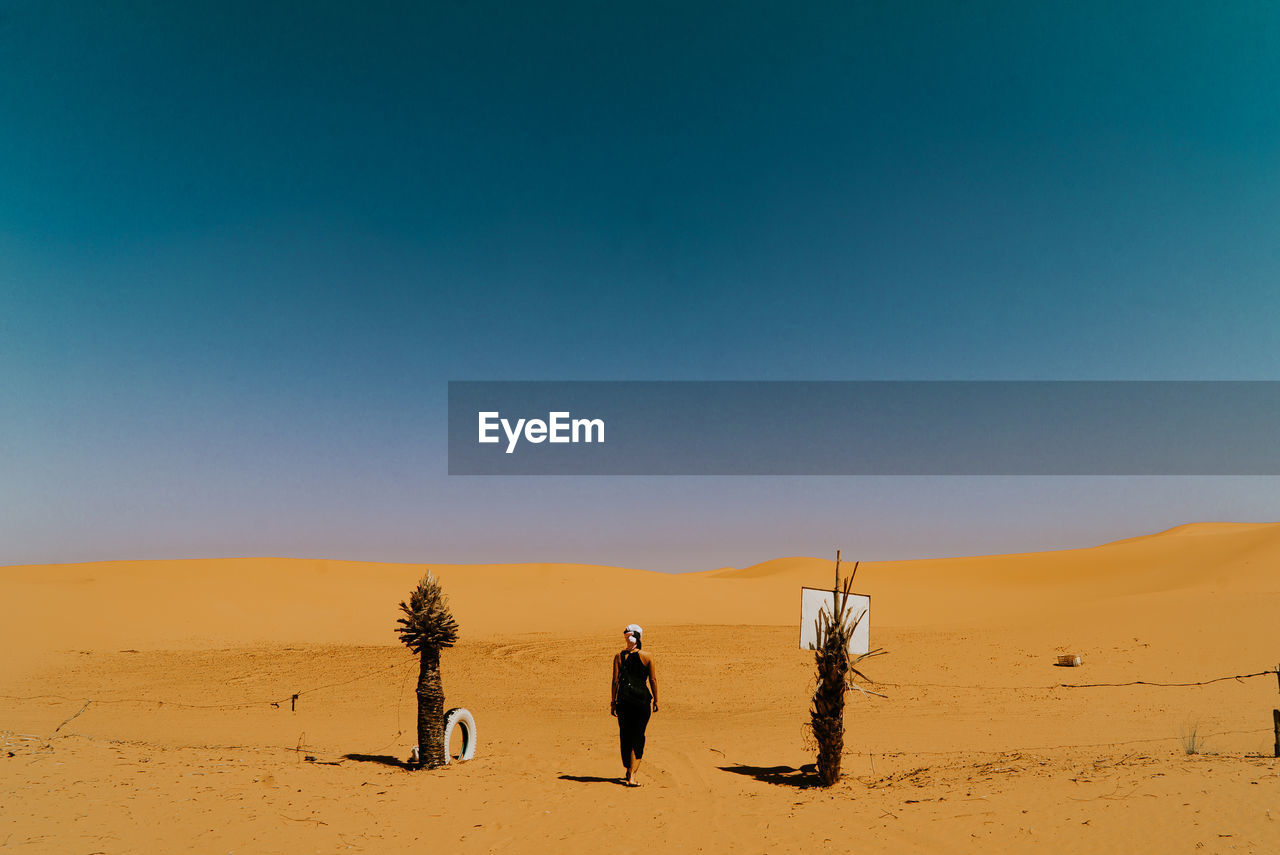 Rear view of woman walking on desert against sky