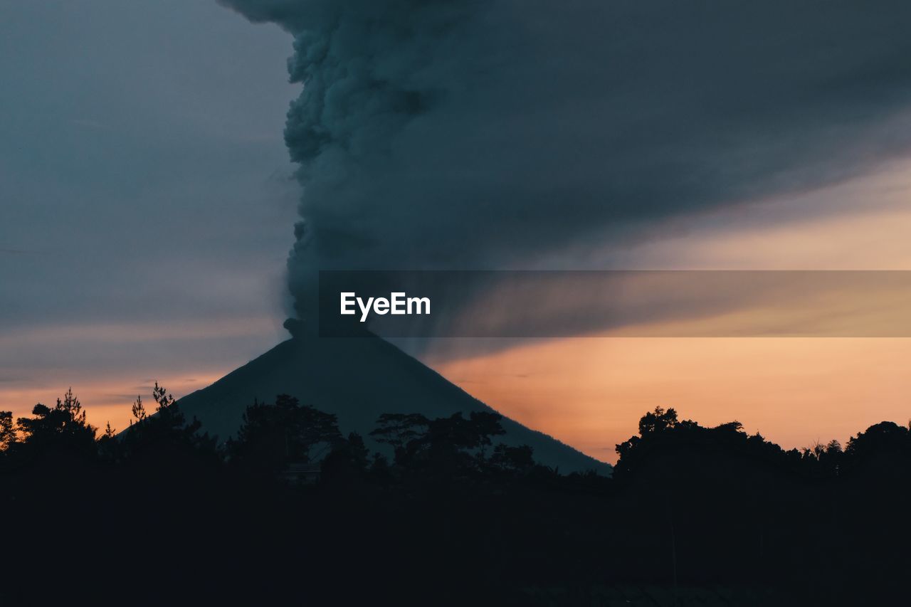 Smoke erupting from mountains against sky during sunset