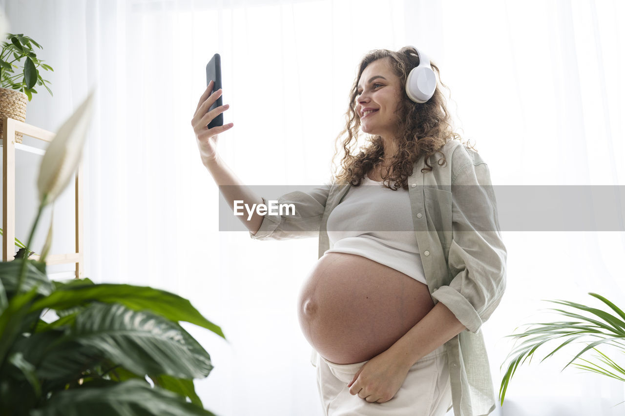 Happy pregnant woman taking selfie through smart phone at home