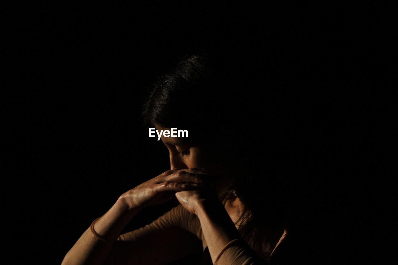 Close-up of woman looking down against black background