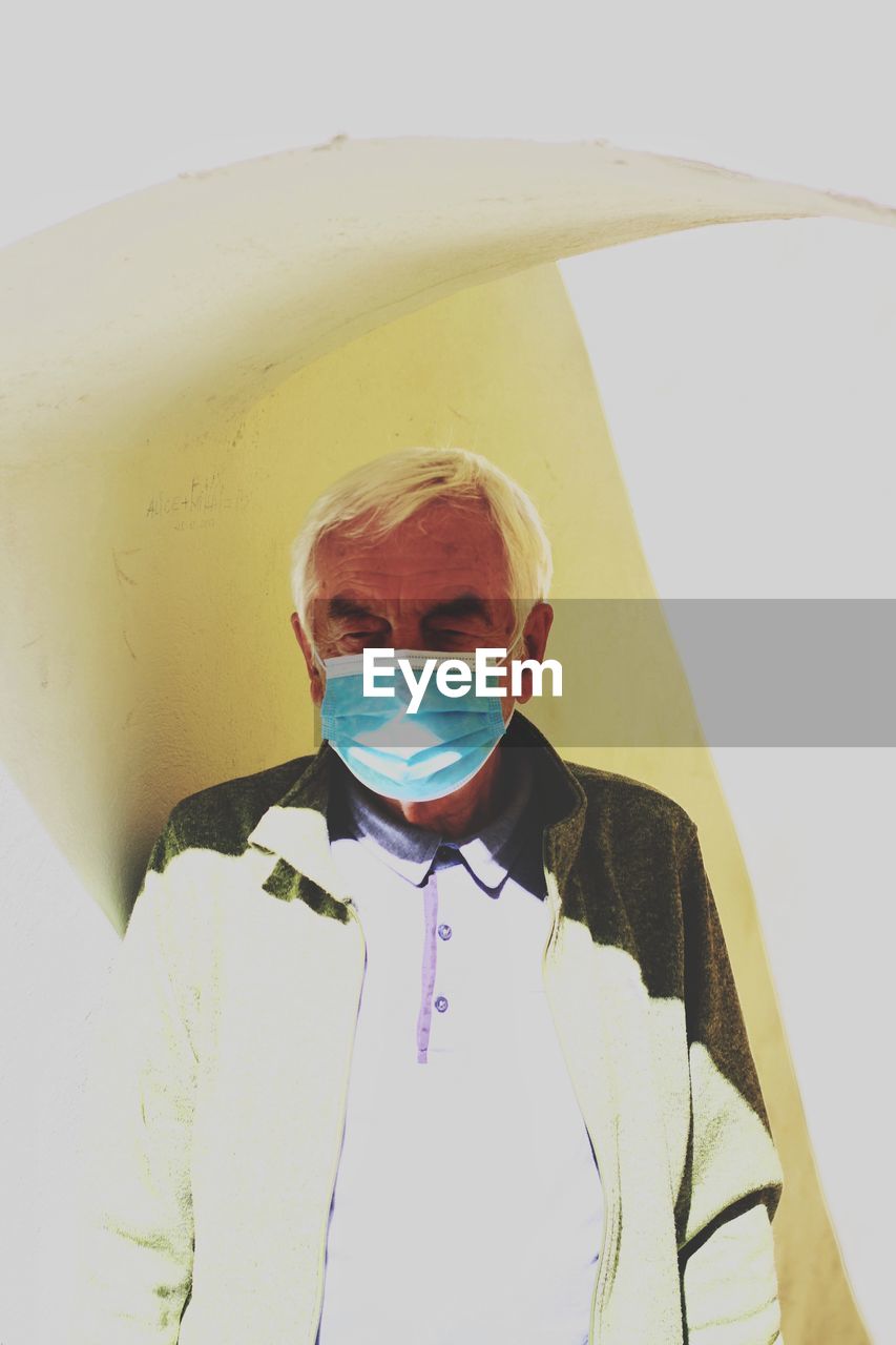 Portrait of man wearing mask standing against white wall on the street