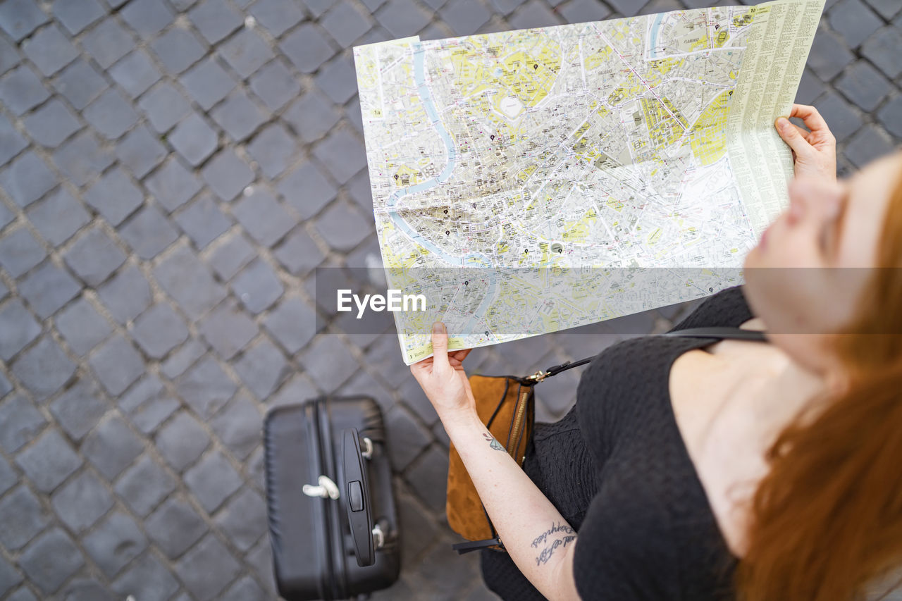 Red hair woman with trolley hold a city map on sanpietrini