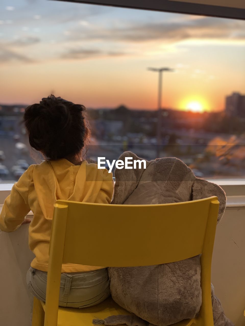 A child watching the sunset next to her doll