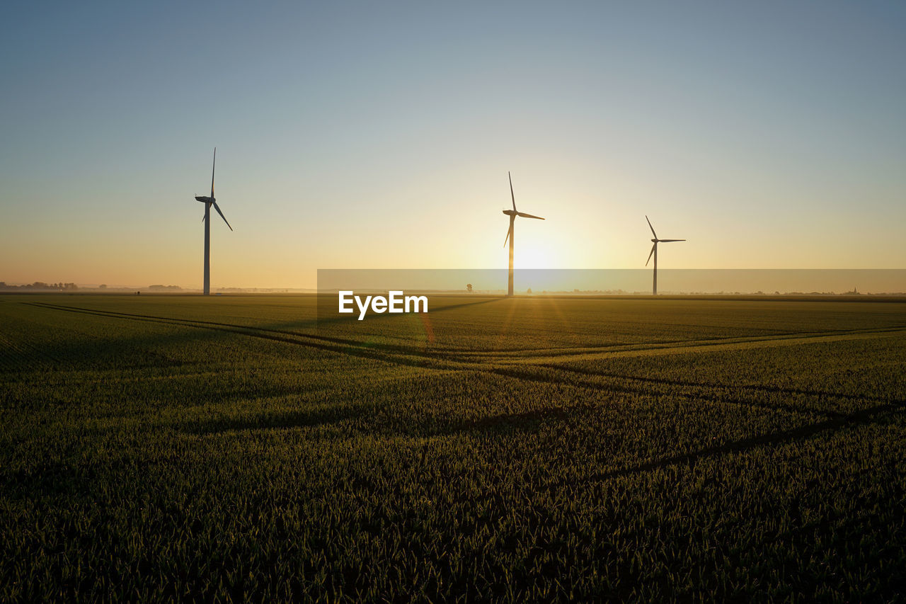 WIND TURBINES ON FIELD AGAINST SKY DURING SUNSET