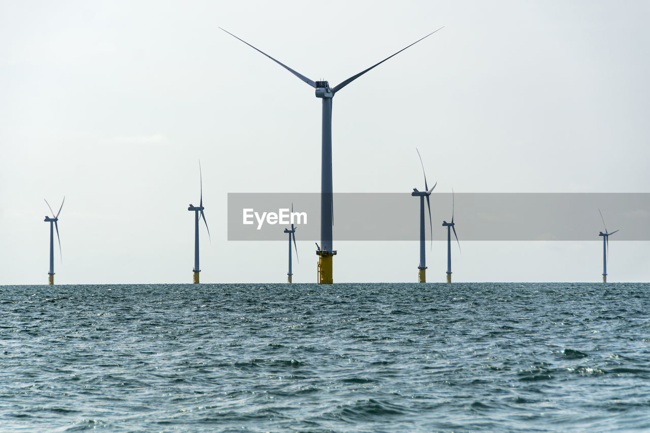 Wind turbines in sea against sky