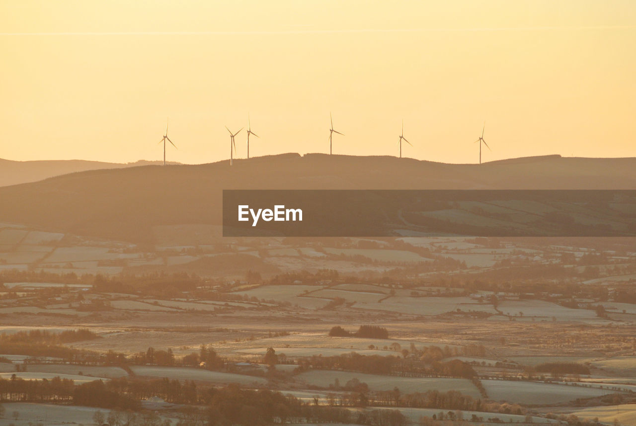 Wind turbines on a ridge silhouetted against an orange dawn sky