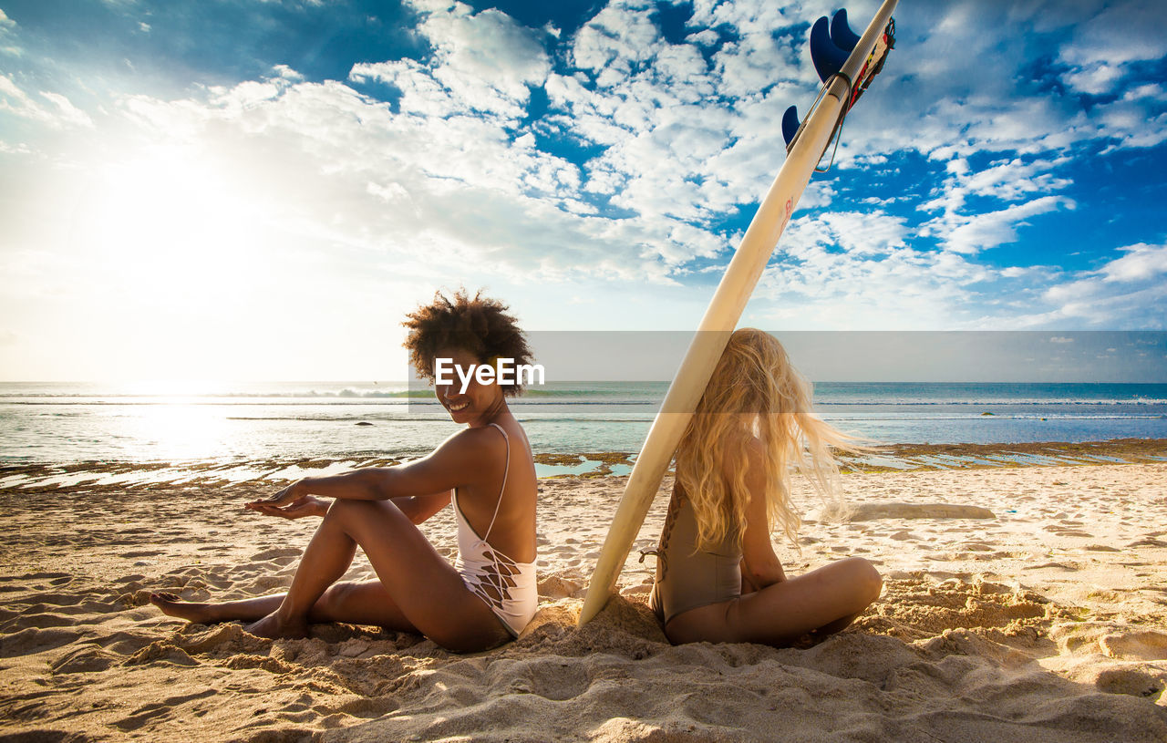 Friends sitting on sand at beach against sky