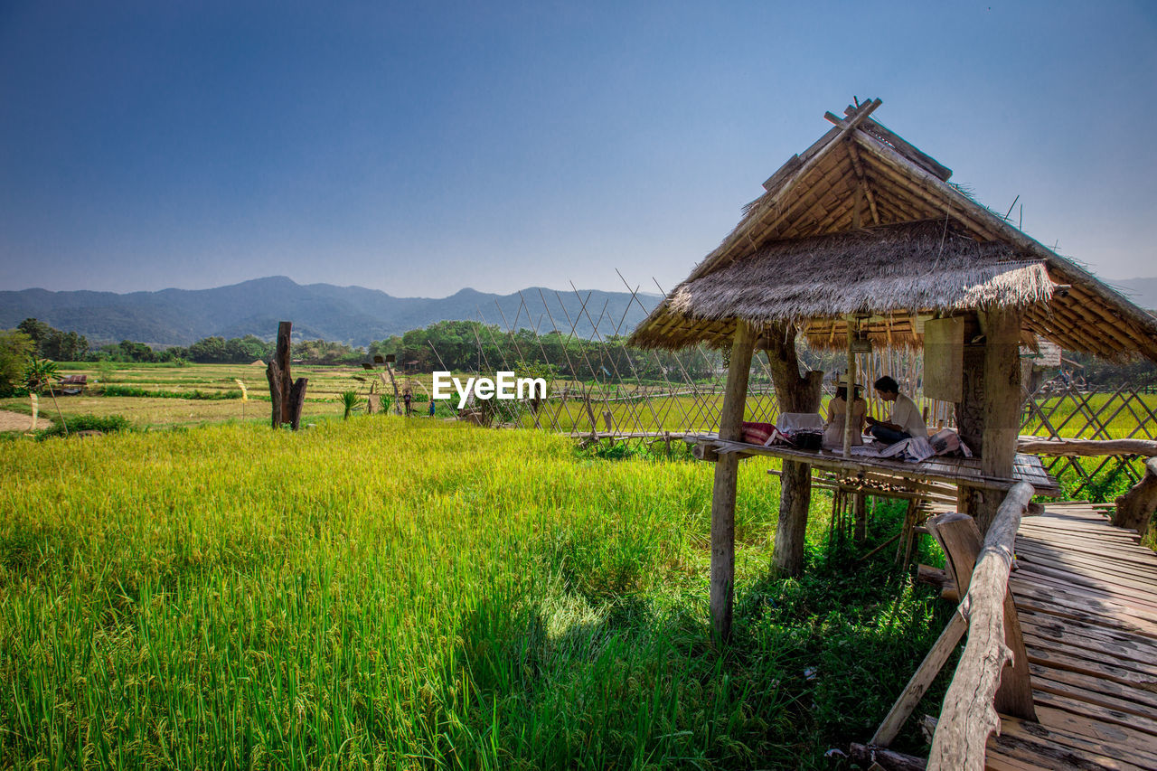 TRADITIONAL WINDMILL ON FIELD BY MOUNTAINS AGAINST SKY