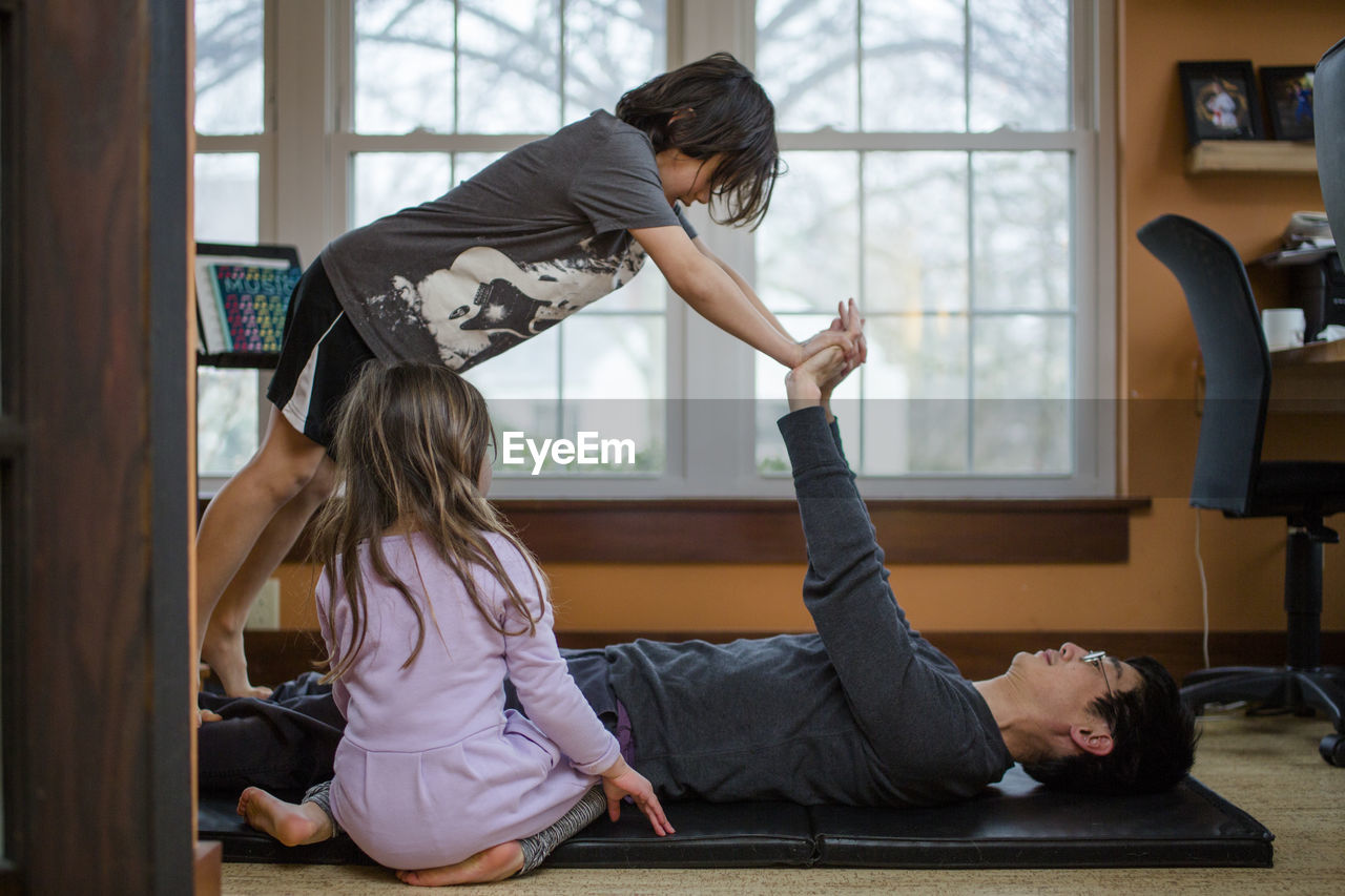 A father does exercise with his two small children inside a home