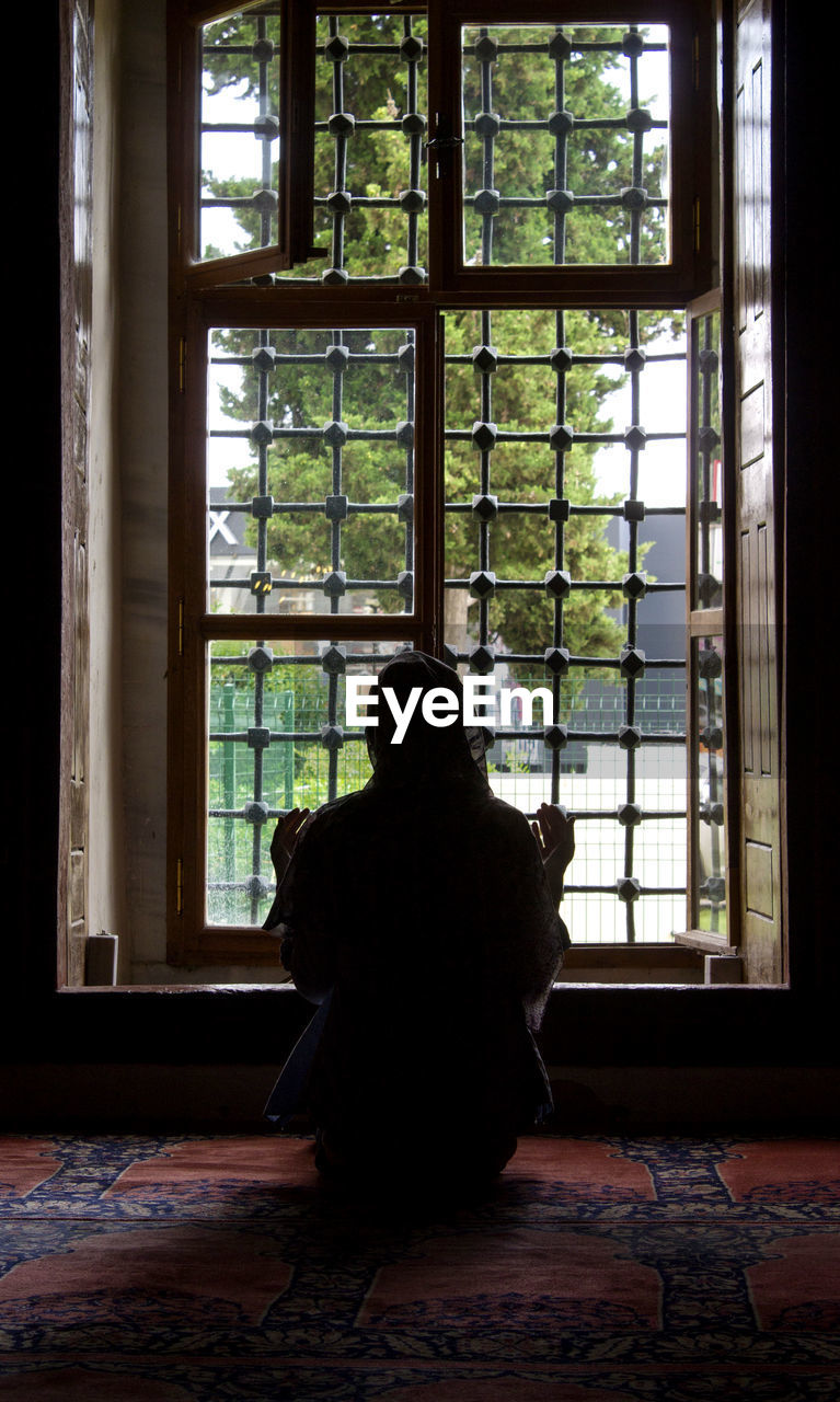 REAR VIEW OF WOMAN SITTING AT WINDOW