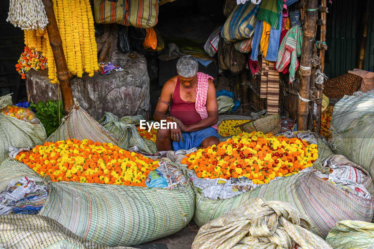 HIGH ANGLE VIEW OF WOMAN SITTING AT MARKET