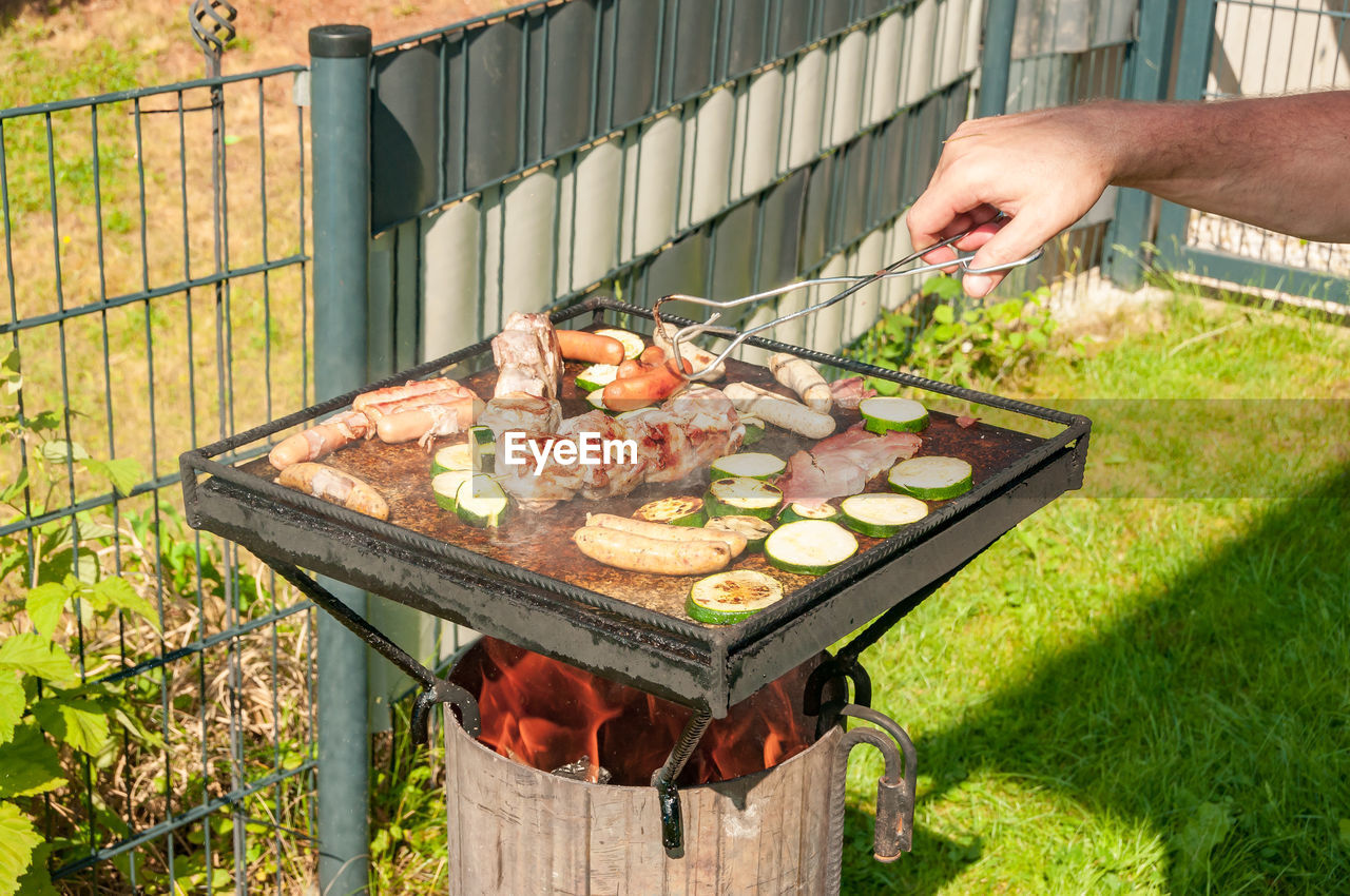 Cropped hand of man cooking meat on barbecue grill in yard