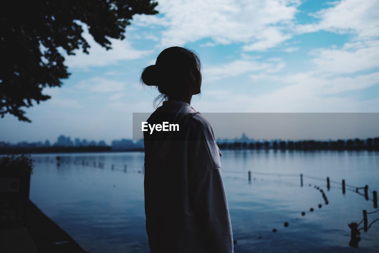 Young woman standing by lake against sky
