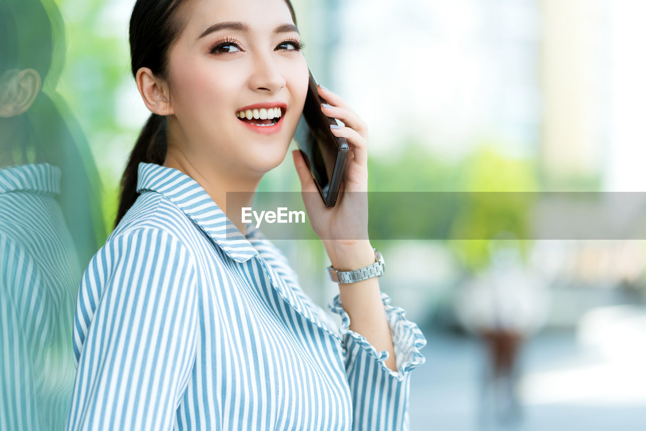 PORTRAIT OF SMILING YOUNG WOMAN USING MOBILE PHONE