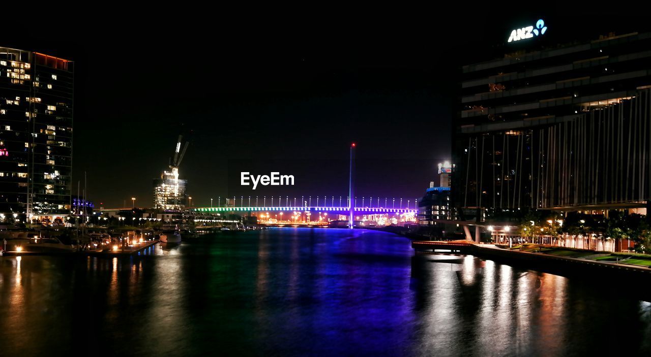 ILLUMINATED BRIDGE OVER RIVER AT NIGHT