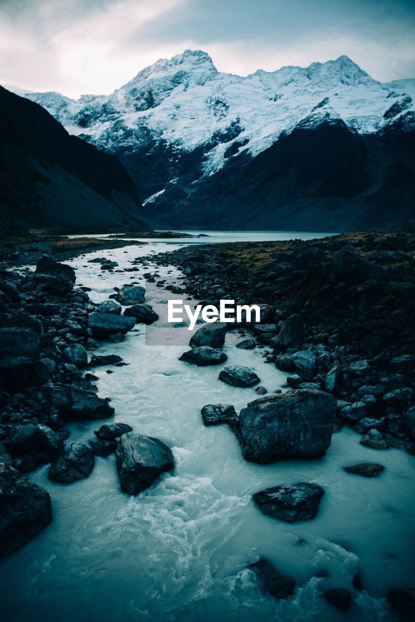 Scenic view of stream and snowcapped mountains against sky