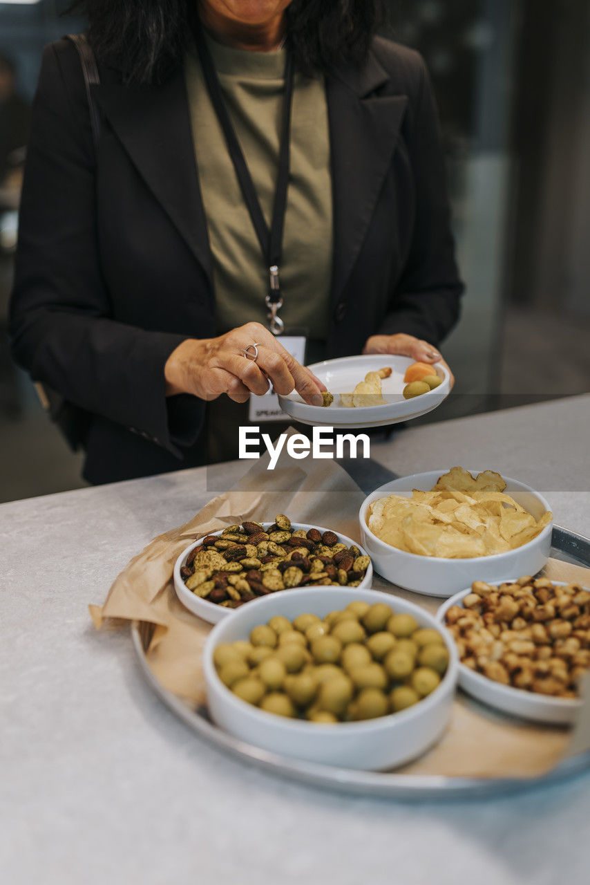 Midsection of senior businesswoman taking snacks in plate during networking event