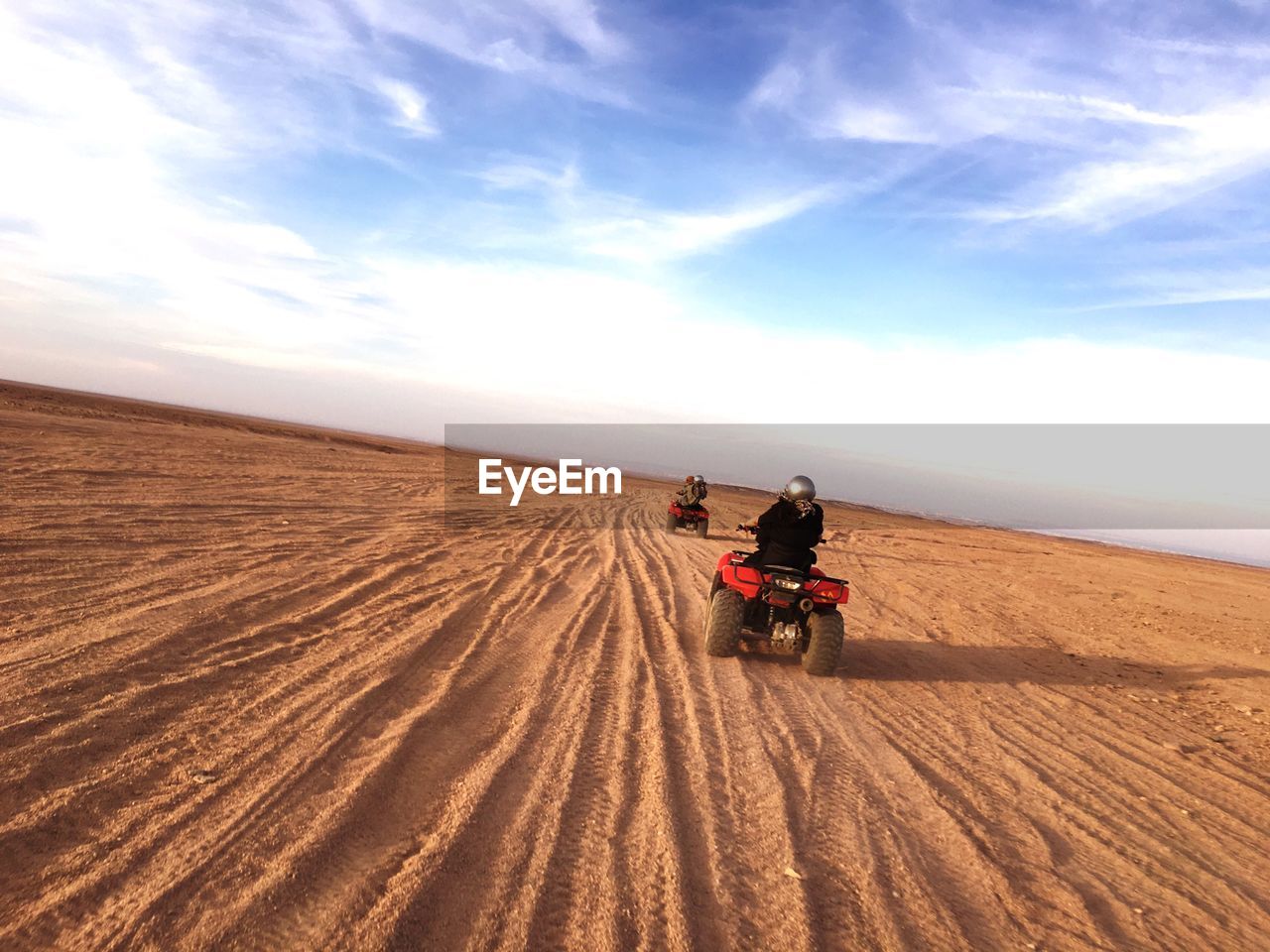 Rear view of people riding quadbikes on desert