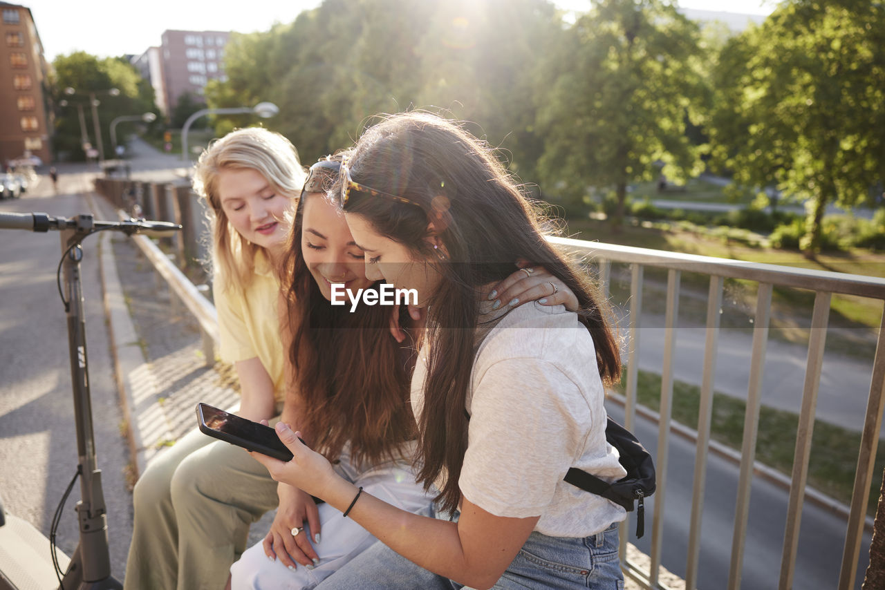 Young female friends spending time together outdoors and using phone