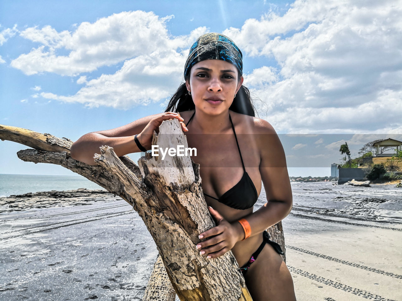 Portrait of woman in bikini sitting on driftwood at beach