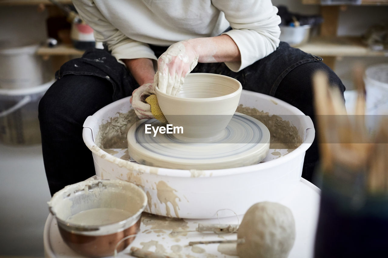 Midsection of mid adult woman molding pot in pottery class
