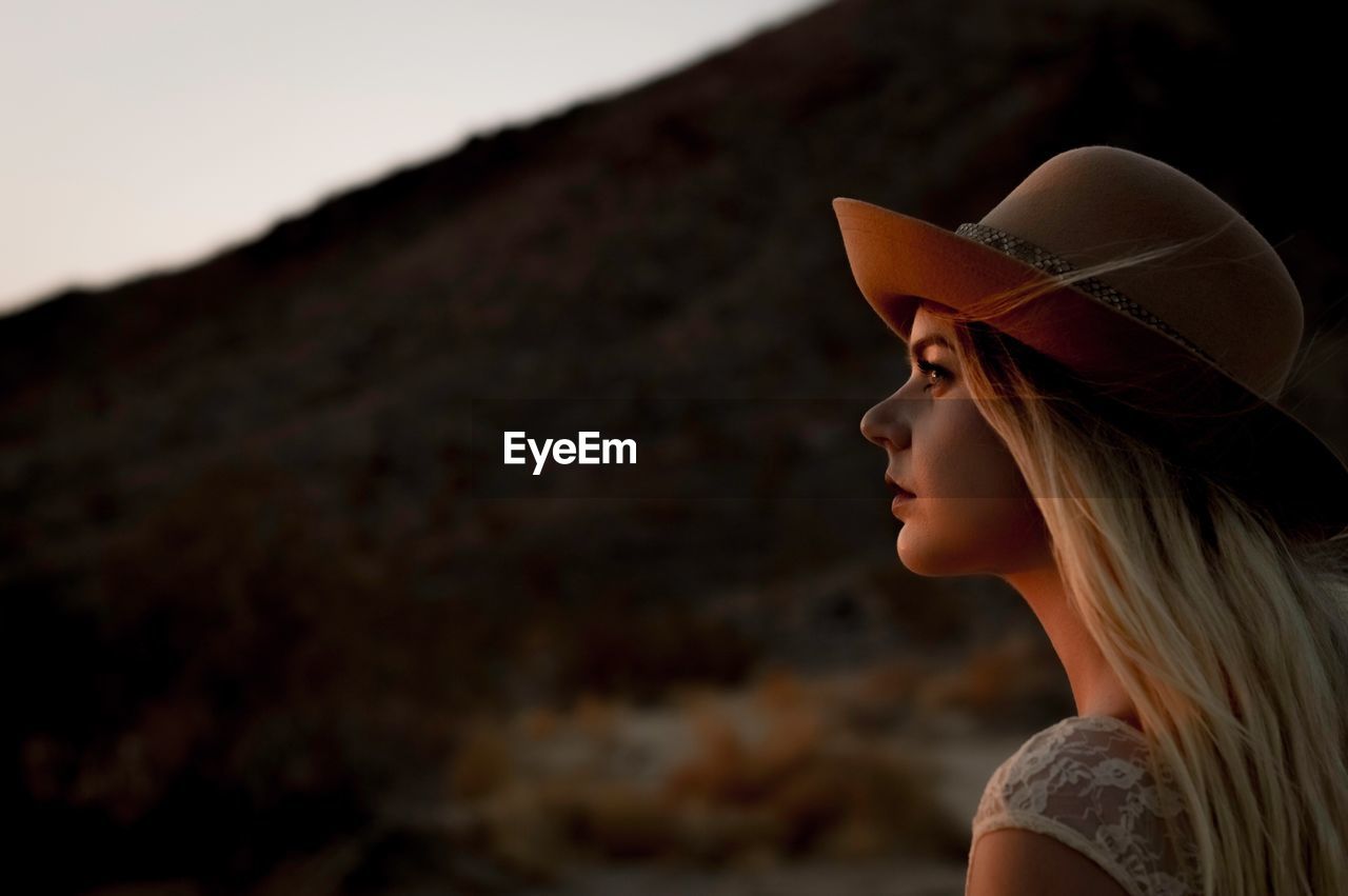 Side view of young woman wearing hat during sunset