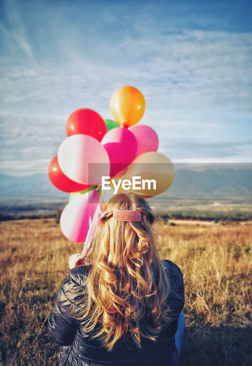 Rear view of woman with colorful balloons sitting on field