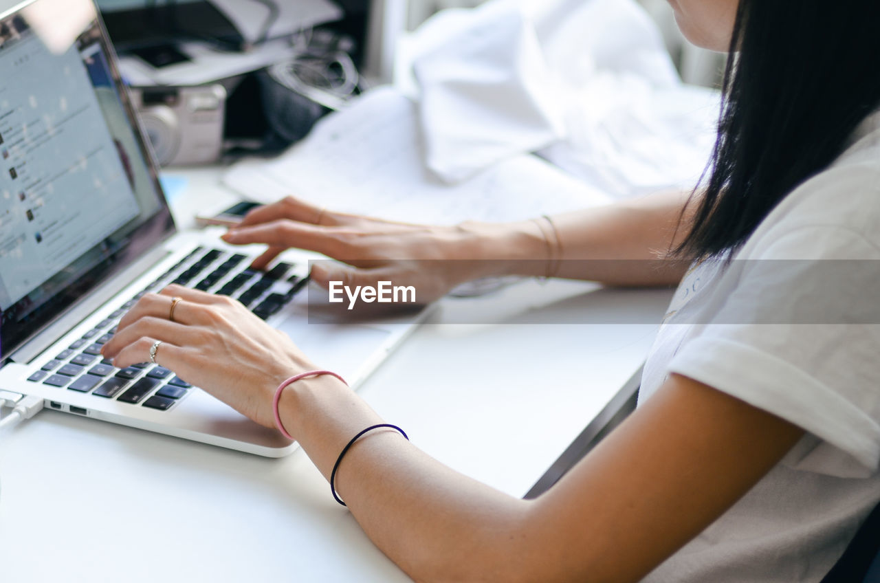 Midsection of woman using laptop at desk in office