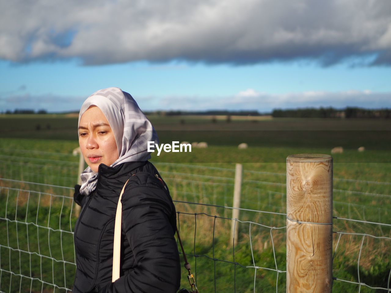 Woman looking away while standing by railing against sky