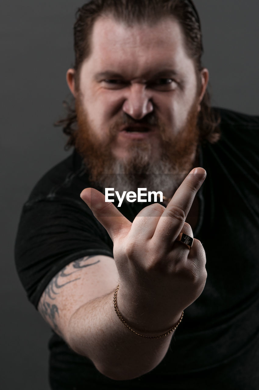 Mid adult man gesturing obscene gesture while sitting against black background