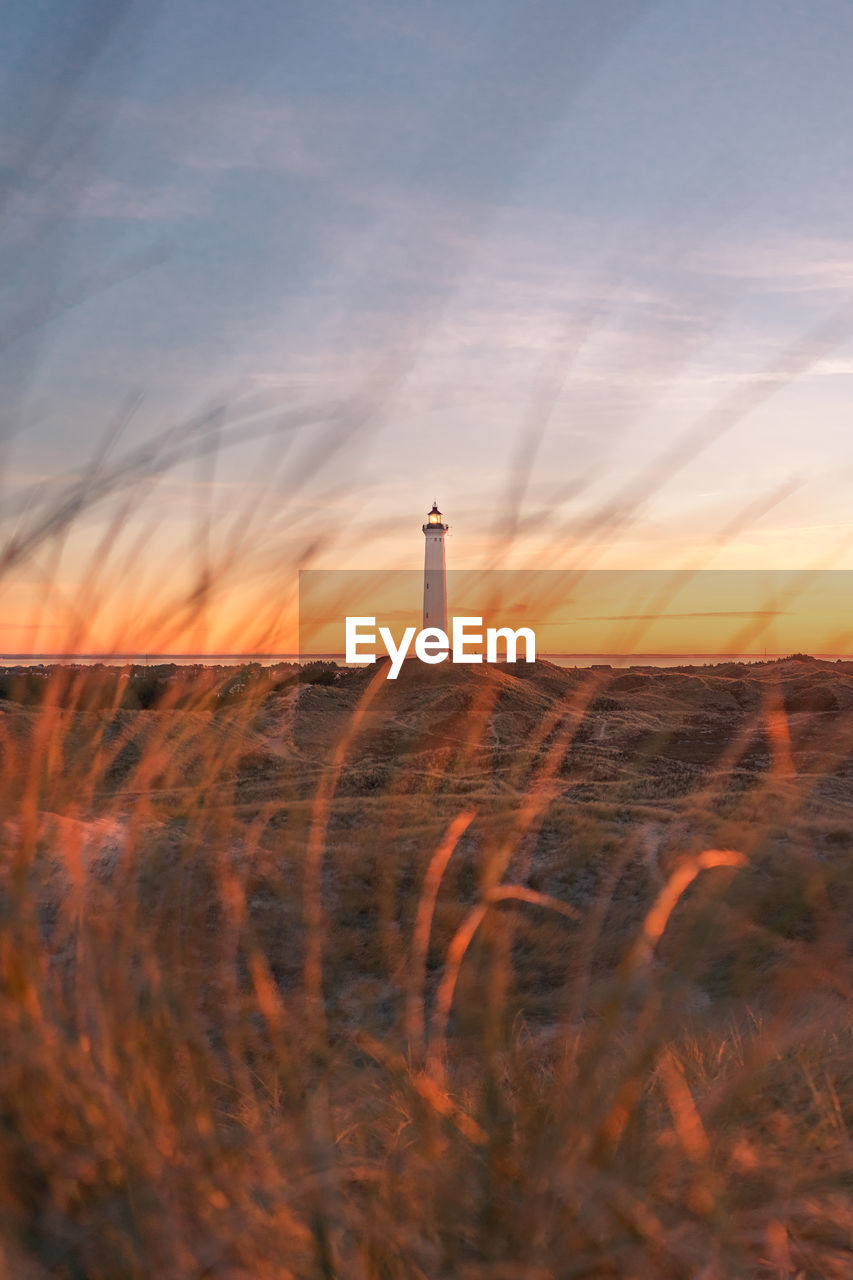 Lighthouse on field against sky during sunset