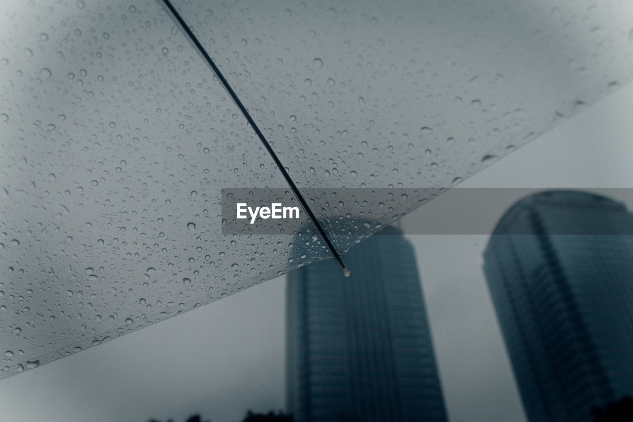 Low angle view of wet umbrella against skyscrapers in city