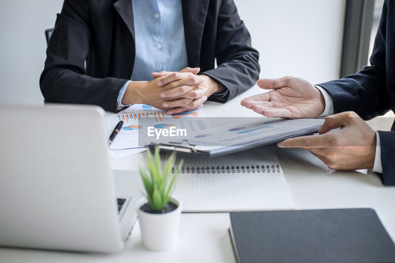 Midsection of and businessman and colleague discussing over graph on table