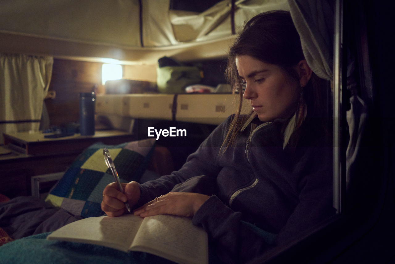 Young woman inside camper writing in journal at night