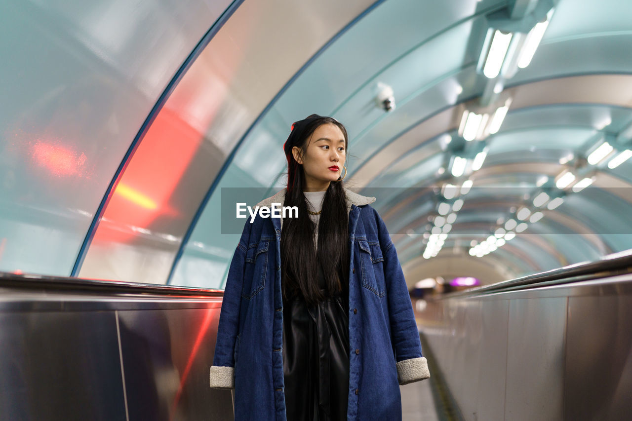 Asian girl in underground. trendy young female in stylish outfit on escalator ride to subway station