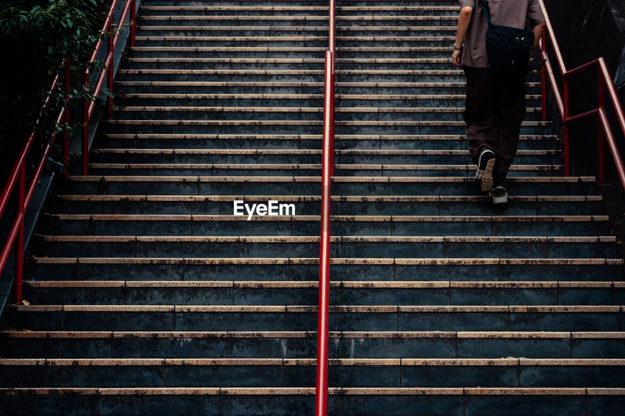 staircase, steps and staircases, stairs, one person, architecture, walking, railing, lifestyles, men, adult, clothing, full length, the way forward, built structure, person, leisure activity, low section, footwear, outdoors, day, casual clothing, rear view, high angle view, on the move, pattern, light, city, standing, line, transportation, wood, women, motion