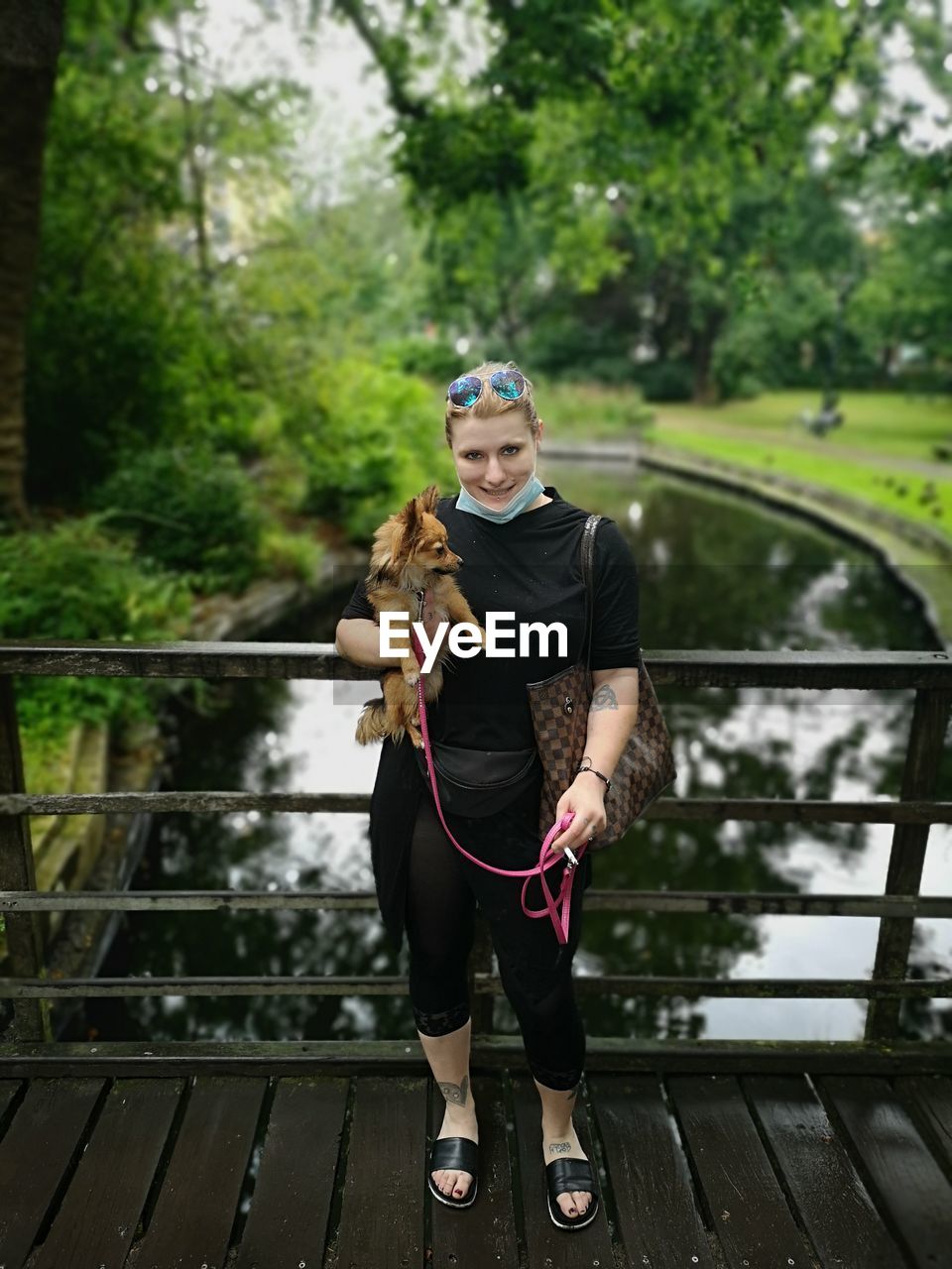 Portrait of young woman carrying puppy while standing on footbridge in park