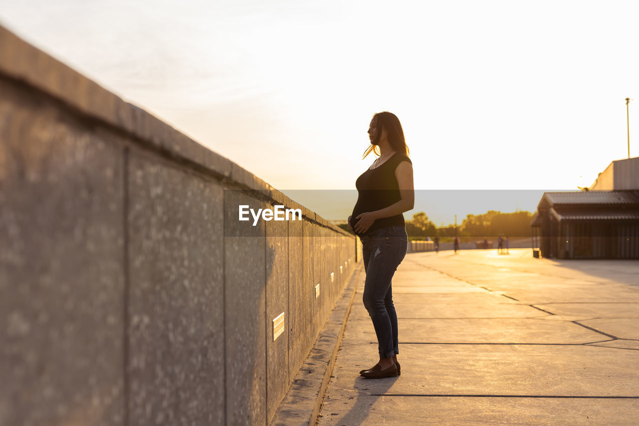 WOMAN STANDING ON FOOTPATH AGAINST WALL