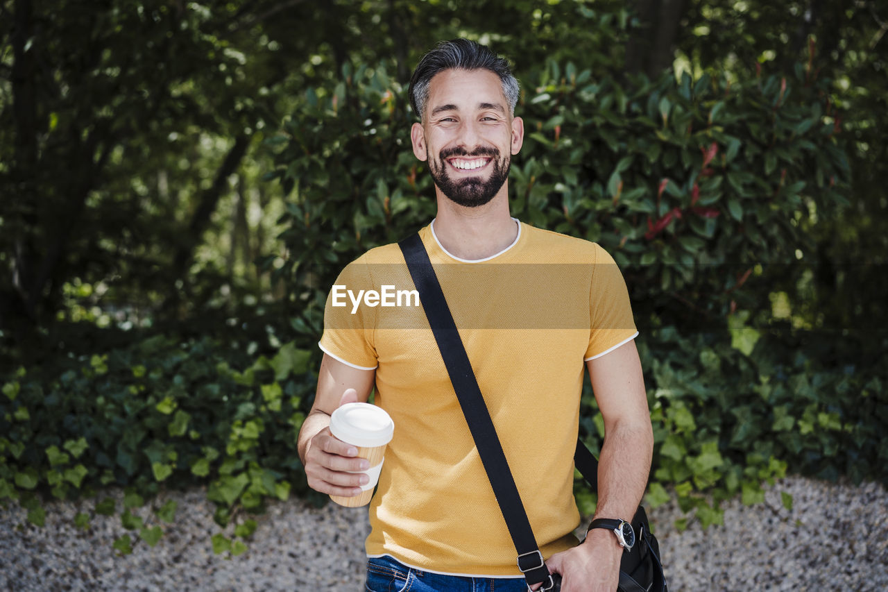 Mid adult man with crossbody bag and disposable cup at park